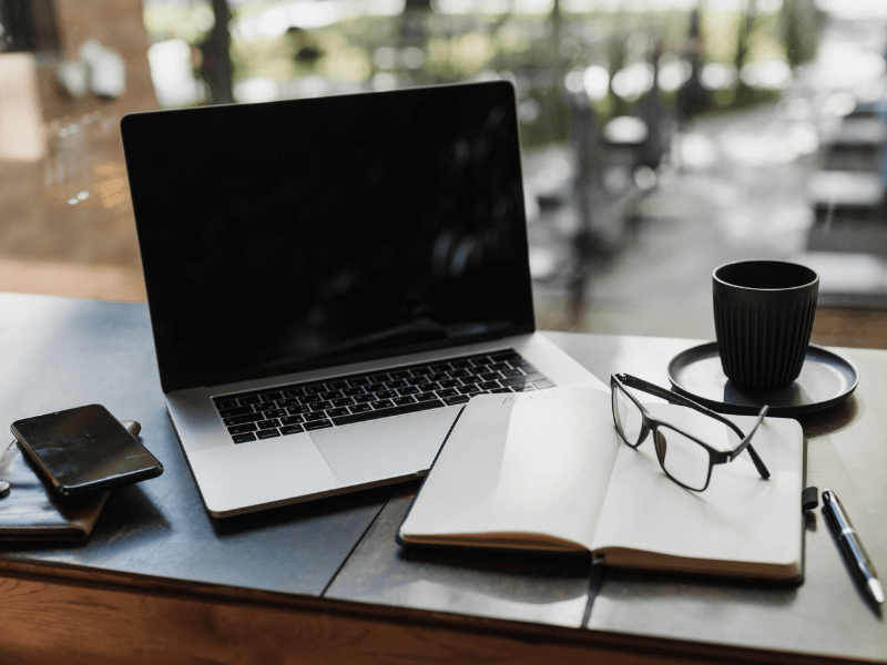 Laptop on desk with a journal and phone
